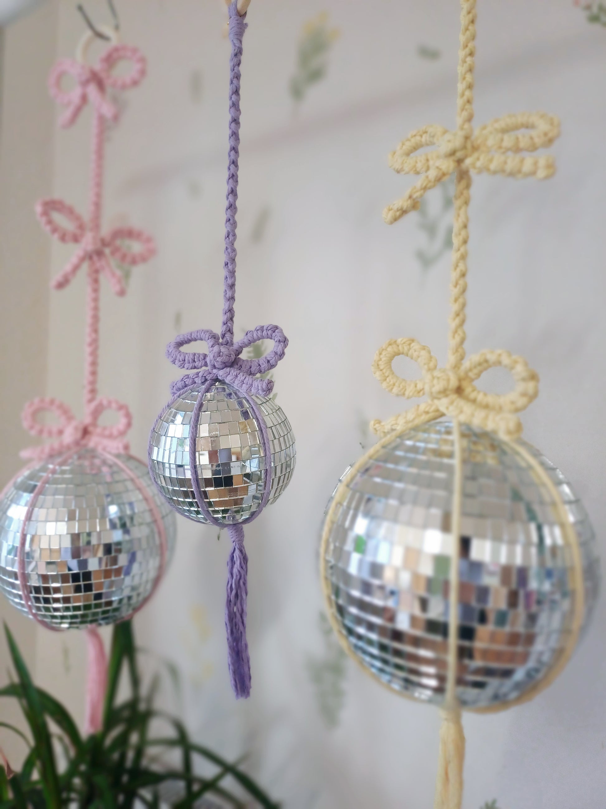 A pink macrame disco ball hanger with a pink bow
